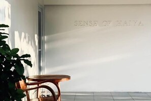 A room with a wooden chair, a white wall with embossed text, and a potted plant. - Sense of Haiya (Chiang Mai)