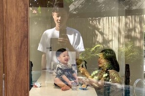 A room with a wooden-framed window, a table with a vase, and a reflection of a person. - Sense of Haiya (Chiang Mai)
