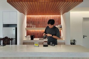 A person preparing a drink at a kitchen counter with a modern design, a coffee maker, and a kettle. - Sense of Haiya (Chiang Mai)