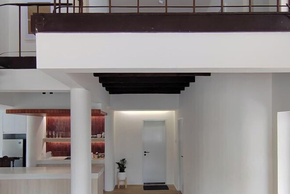 Een modern interieur met een trap naar een balkon, een keukenhoek en een woonruimte met een rode accentmuur.