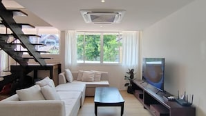 A modern living room with a sofa, coffee table, TV, and staircase. - Sense of Haiya (Chiang Mai)