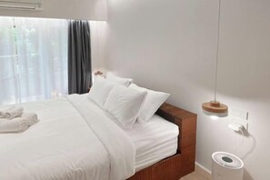 Een net opgemaakt bed met witte lakens, een nachtkastje met een lamp en een luchtzuiveraar aan de muur.