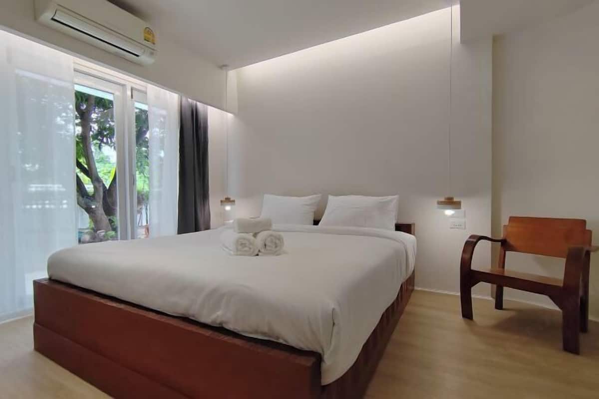 Une chambre à coucher moderne avec un grand lit, un banc en bois et une vue sur la verdure par la fenêtre.