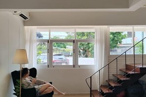 A room with a large window, a chair, a lamp, and a staircase. - Sense of Haiya (Chiang Mai)