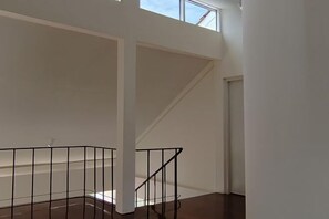 A spacious interior with a high ceiling, a staircase with black railings, and a door leading to another room. - Sense of Haiya (Chiang Mai)