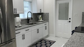 A modern kitchen with white cabinets, a stainless steel refrigerator, granite countertops, and a patterned rug. - Gulf Access Getaway in Punta Gorda (Punta Gorda)