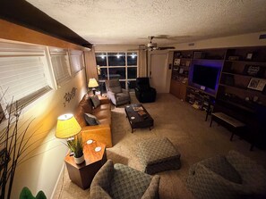 A living room with a sofa, armchairs, a coffee table, a TV, and a bookshelf.
