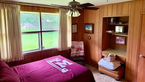 A bedroom with a queen-sized bed, wooden paneling, a ceiling fan, a window with curtains, and a bookshelf with framed pictures. - NEAR CAMPUS! Choice KING or QUEEN BEDS w fresh interior paint & great parking! (College Station)
