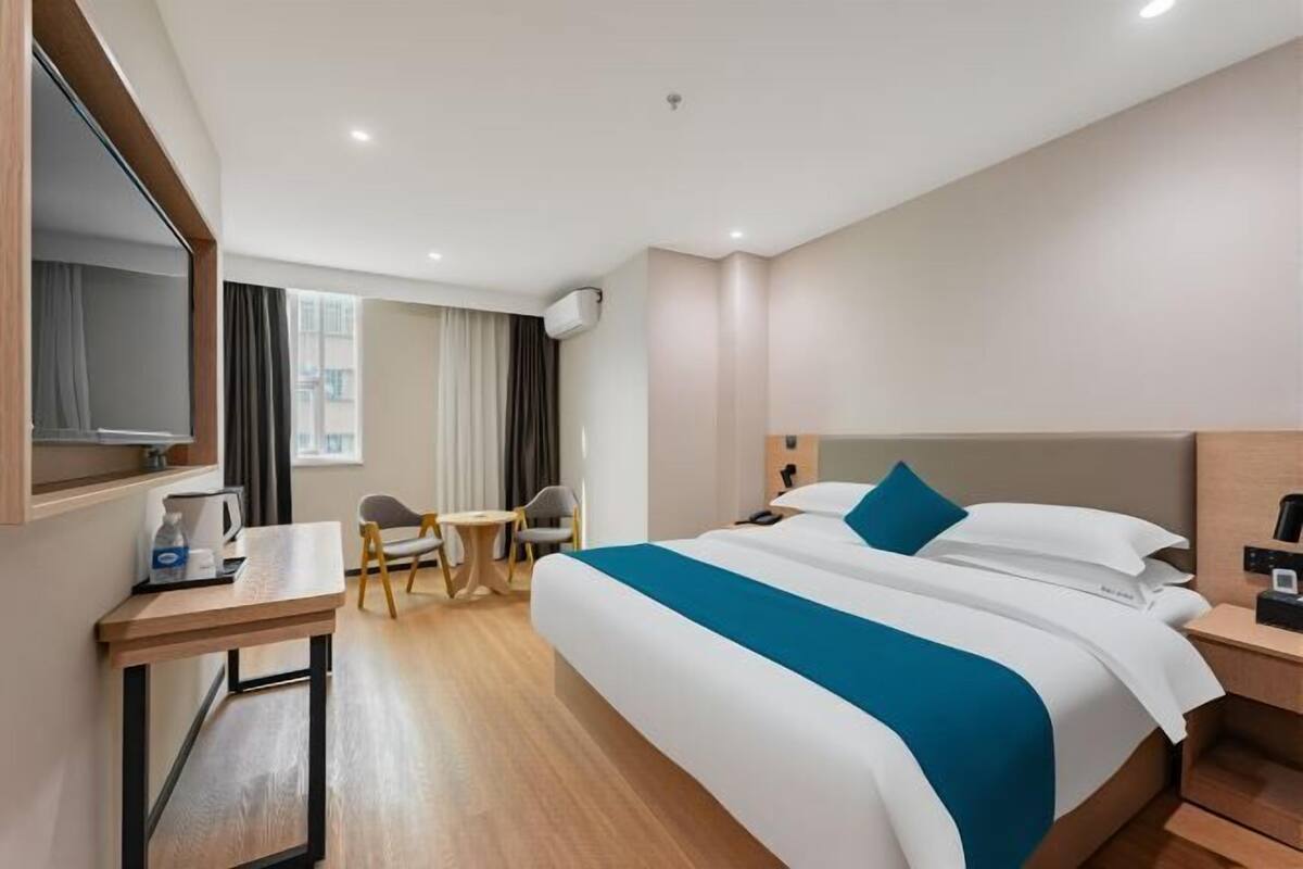A hotel room with a large bed, a desk, a chair, a small table, and a TV.