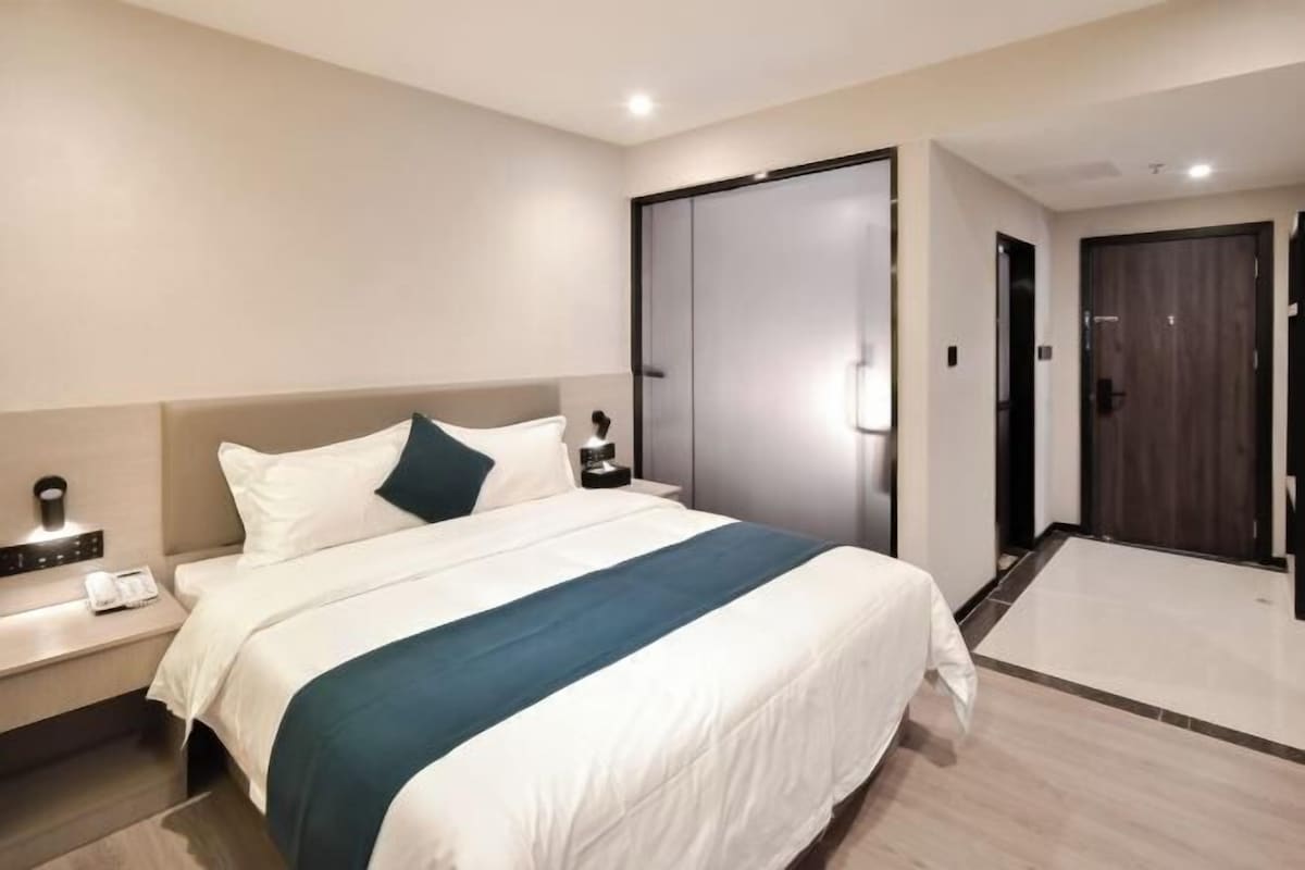 Ein Hotelzimmer mit einem großen Bett, einem Nachttisch mit Telefon, einem Kleiderschrank und einer Tür zu einem anderen Raum.