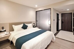 Ein Hotelzimmer mit einem großen Bett, einem Nachttisch mit Telefon, einem Kleiderschrank und einer Tür zu einem anderen Raum.