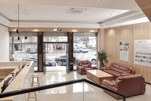 A hotel lobby with a reception desk, seating area, and a view of the street through large glass doors. - Shell Hotel (Zhuhai Doumen Daxin Xinduhui) (Zhuhai)