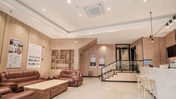 A modern hotel lobby with leather sofas, a reception desk, a staircase, and a wooden wall display. - Shell Hotel (Zhuhai Doumen Daxin Xinduhui) (Zhuhai)