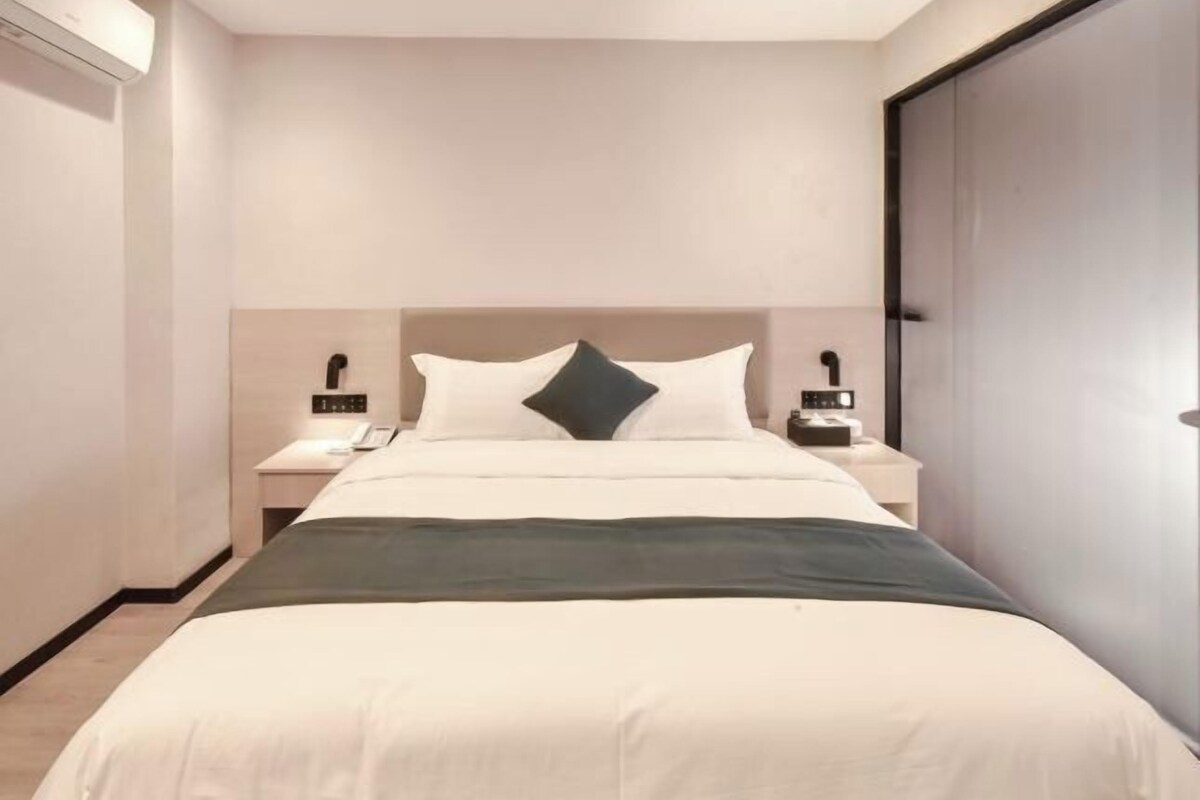 Ein modernes Hotelzimmer mit einem großen Bett, Nachttischen, einem Beistelltisch und einem Kleiderschrank.