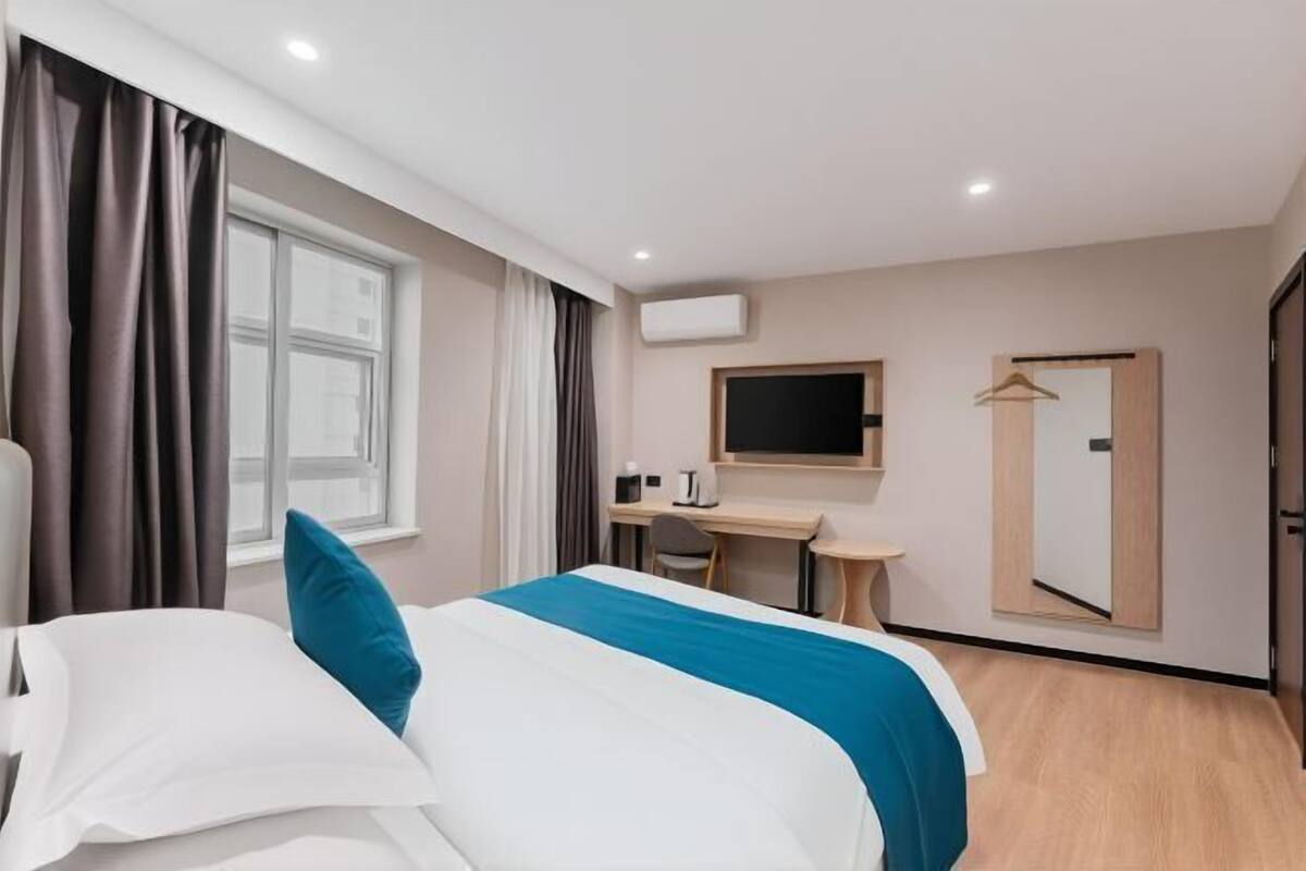 A hotel room with a bed, a desk, a chair, a TV, and a wardrobe.