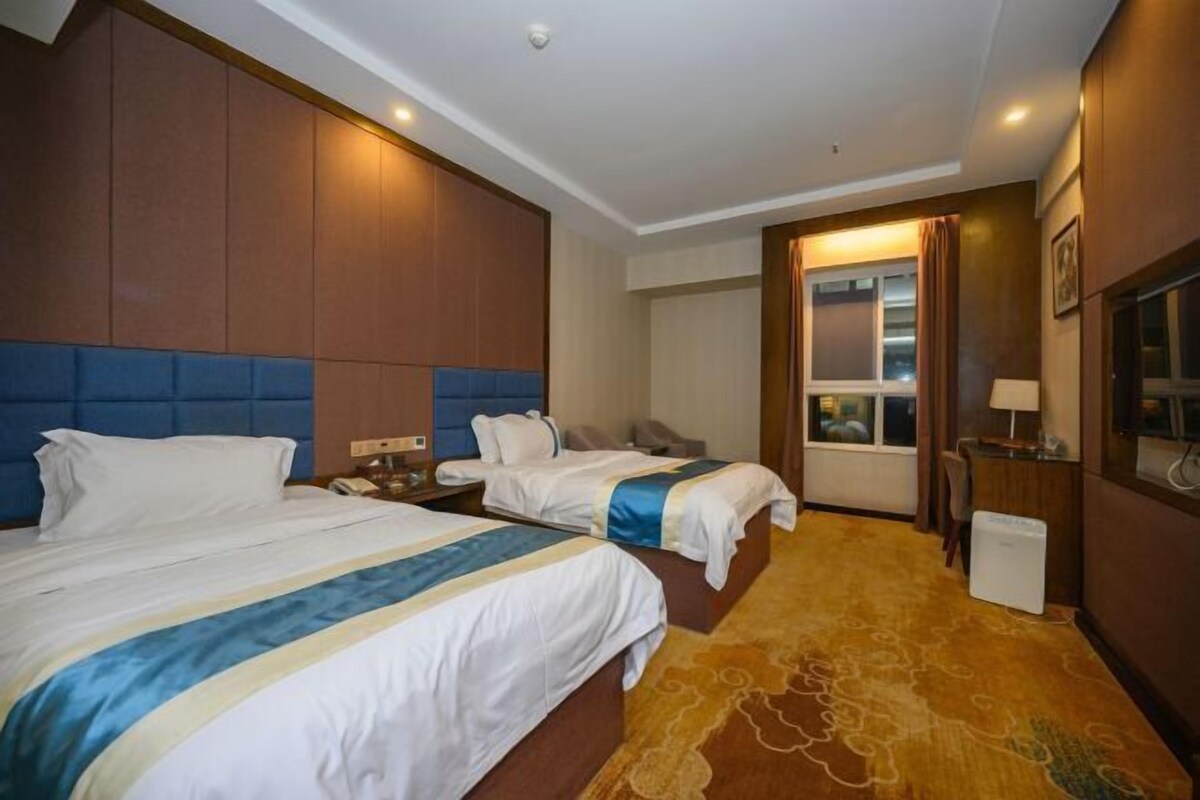 A hotel room with two beds, a large window, a television, and a desk with a lamp.