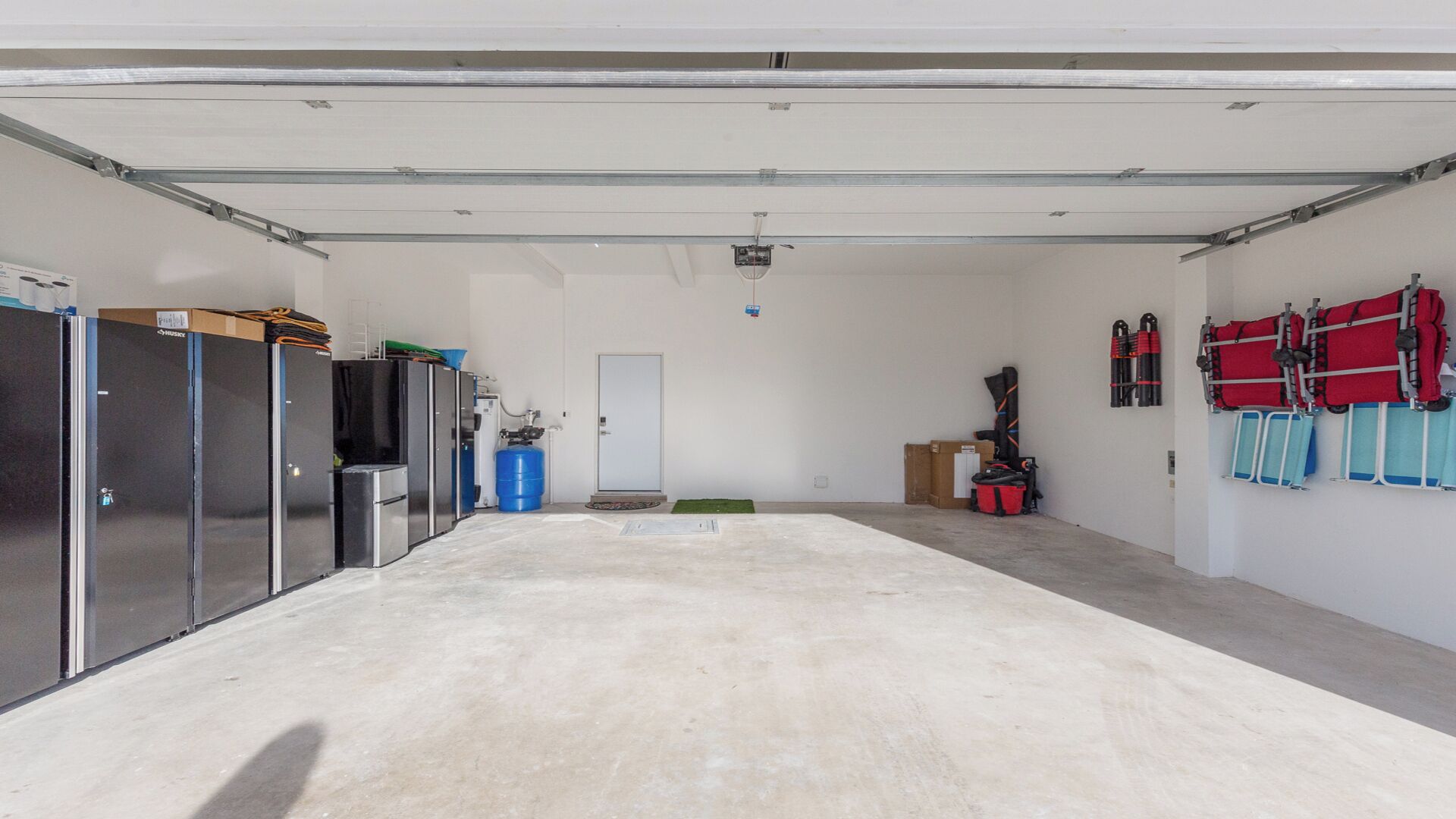 A clean, empty garage with a concrete floor, a white door, and storage cabinets on the left.