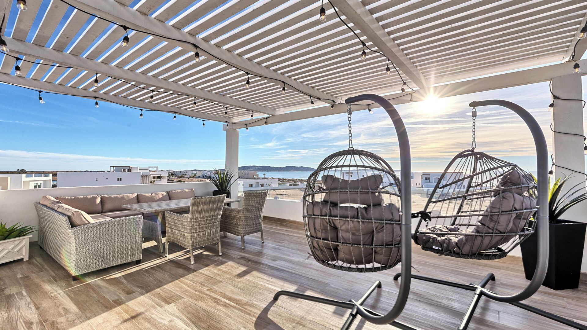 Una terraza en la azotea con mobiliario de mimbre, sillones colgantes y vista al mar.