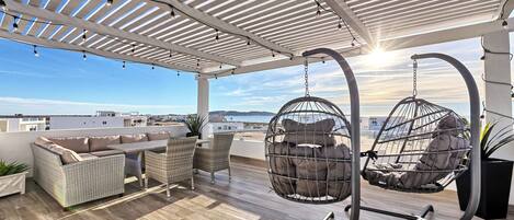 Una terraza en la azotea con mobiliario de mimbre, sillones colgantes y vista al mar.