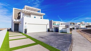 Un complejo residencial moderno con varias edificaciones blancas, un camino pavimentado y césped artificial verde.