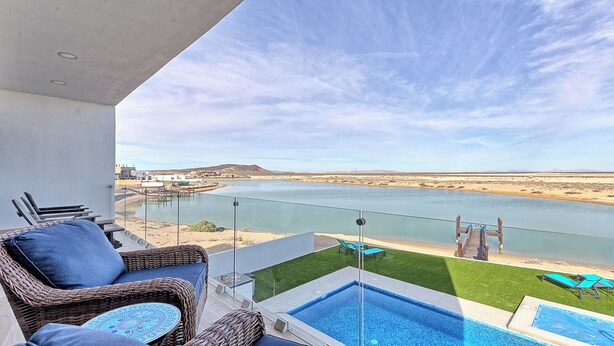 Un balcón con vistas a un río, una piscina y mobiliario exterior.