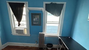 A bedroom with a bed, a desk, and two windows with curtains. - Fidelia Room Fuchsite (Irvington)