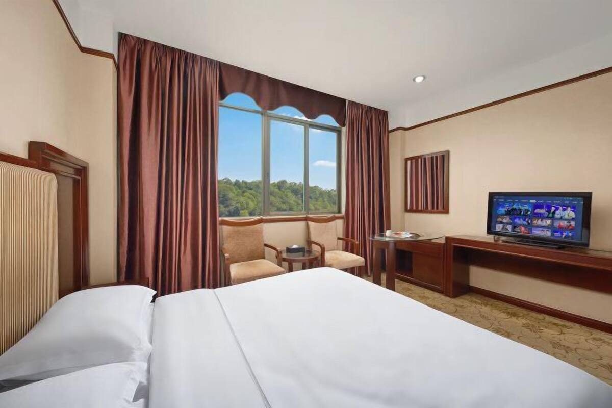 A hotel room with a bed, a desk, a television, and a window with curtains.