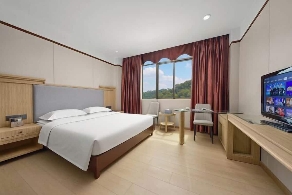 A hotel room with a bed, a desk, a chair, a TV, and a window with curtains.