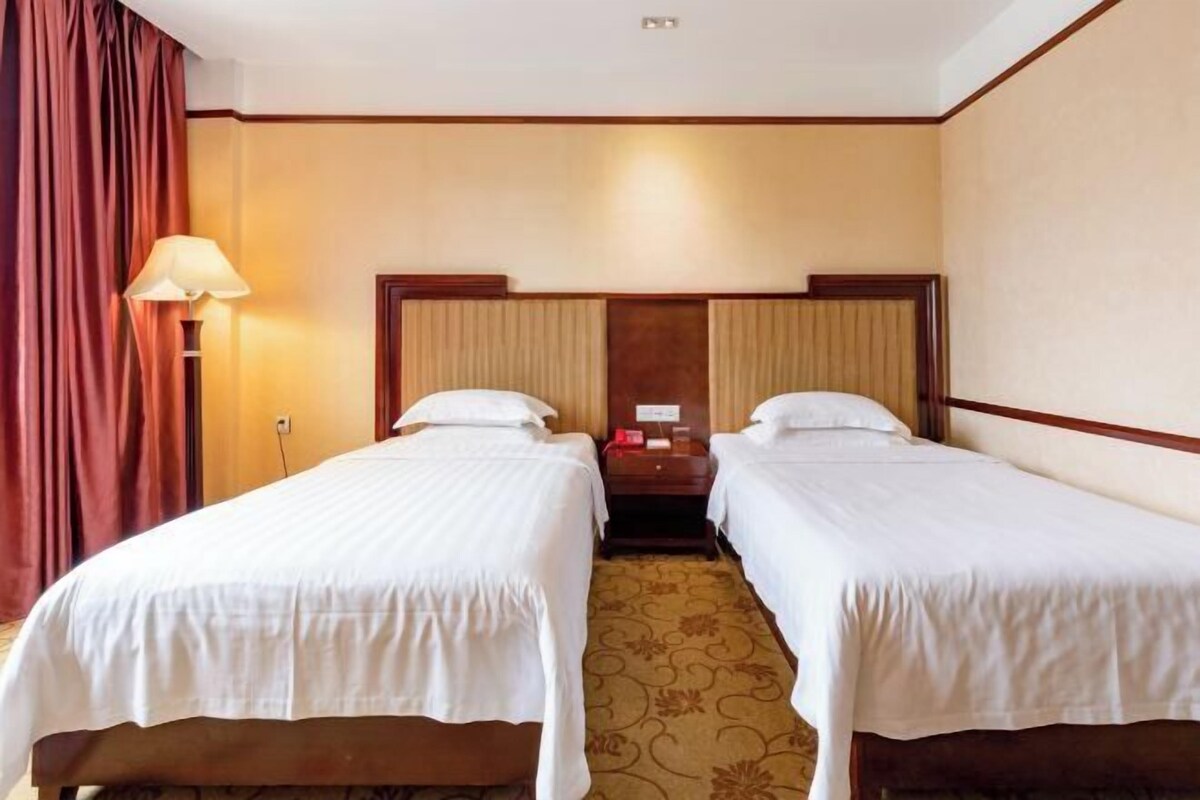 Una habitación de hotel con dos camas individuales, una mesita de noche, una lámpara y piso alfombrado.