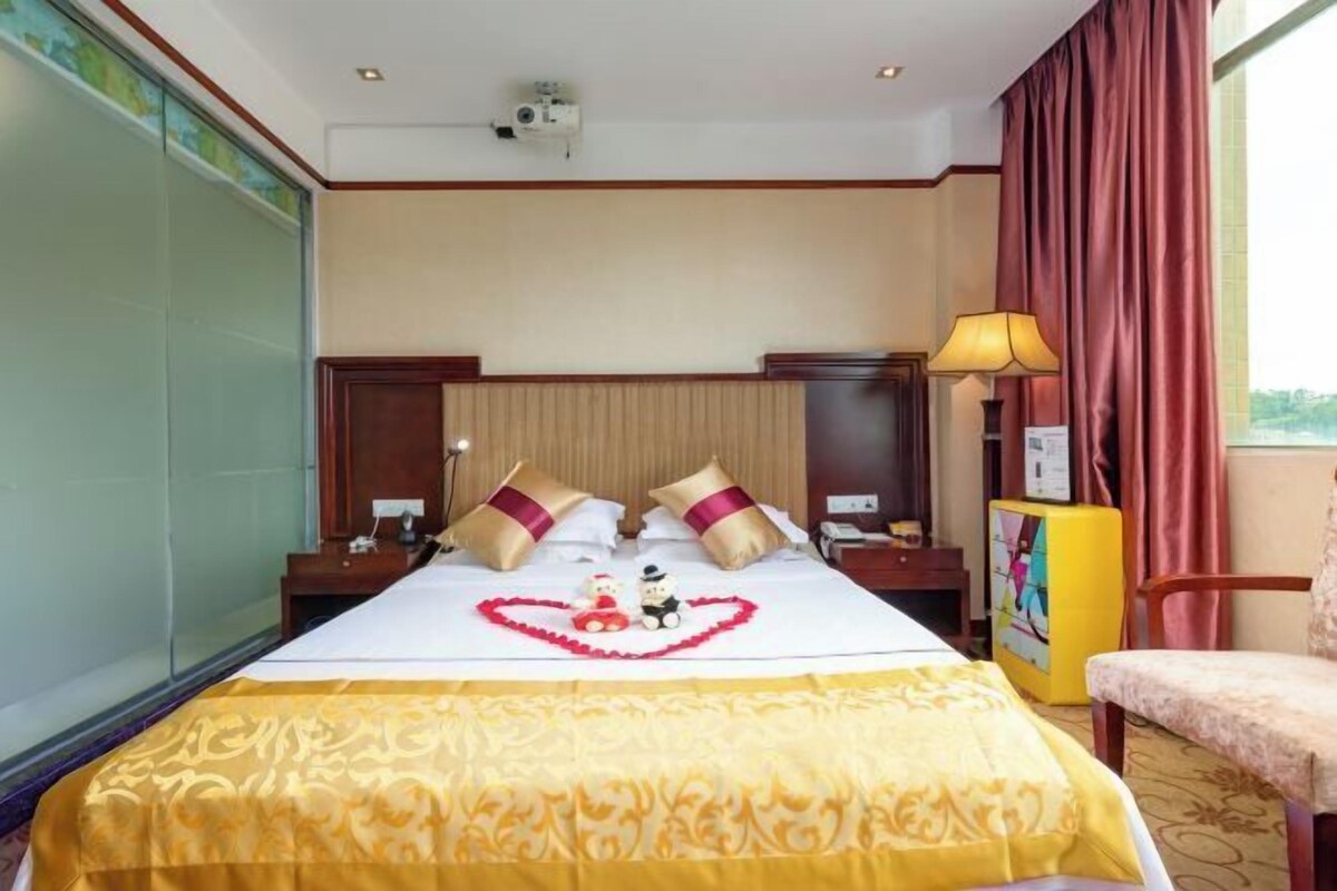 Habitación de hotel con cama, mesita de noche, lámpara, silla y ventana con cortinas.