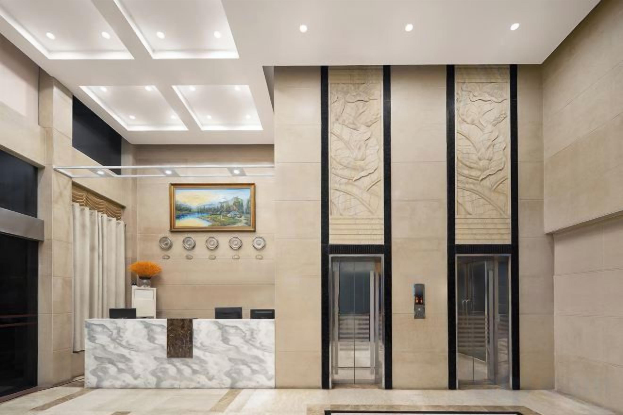 Ein Hotel-Empfangsbereich mit einem мраморнем Empfangstresen, einem Gemälde und einem modernen Aufzug.