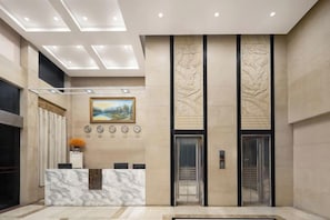 A hotel reception area with a marble reception desk, a painting, and a modern elevator. - Yinwan Hotel( South China country garden store) (Guangzhou)