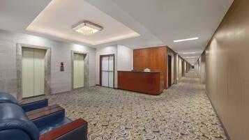 Un vestíbulo de hotel con una recepción, dos ascensores y una alfombra estampada.