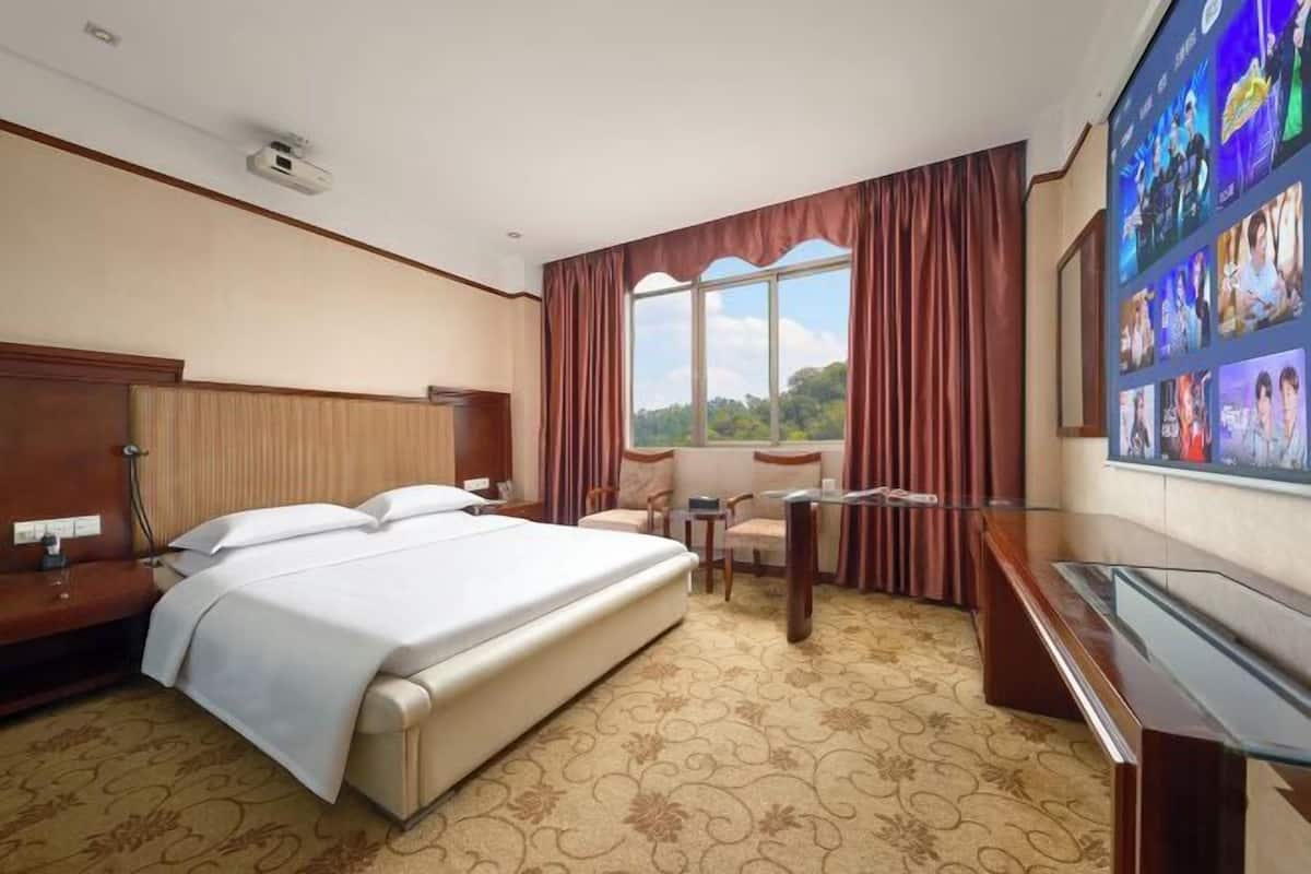 A hotel room with a bed, a desk, a chair, and a large window with curtains.