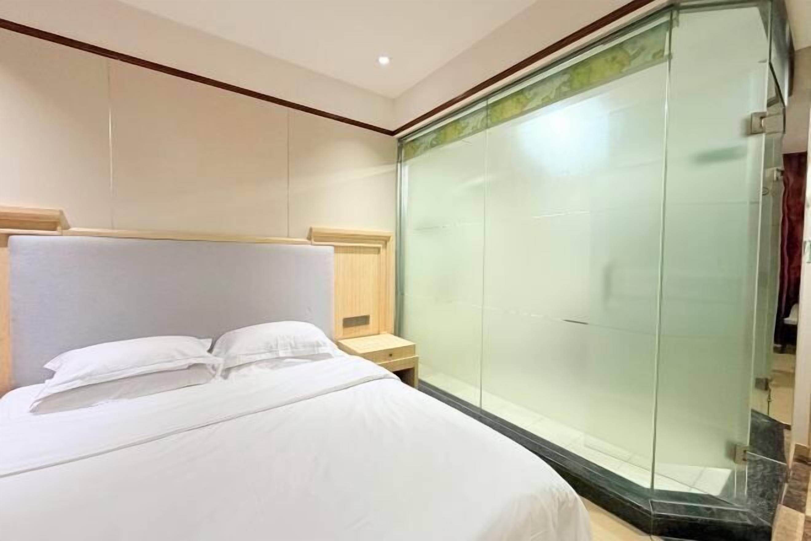 Habitación de hotel con cama, mesita de noche y ducha con mampara de vidrio.
