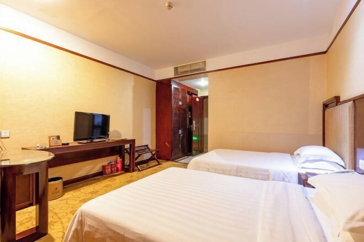 Una habitación de hotel con dos camas, un escritorio con televisor y una mesita.
