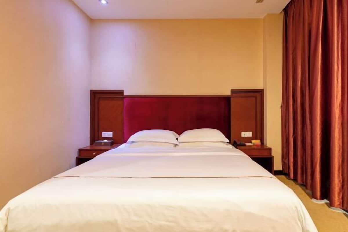 A hotel room with a large bed, wooden headboard, two bedside tables, and a red curtain.