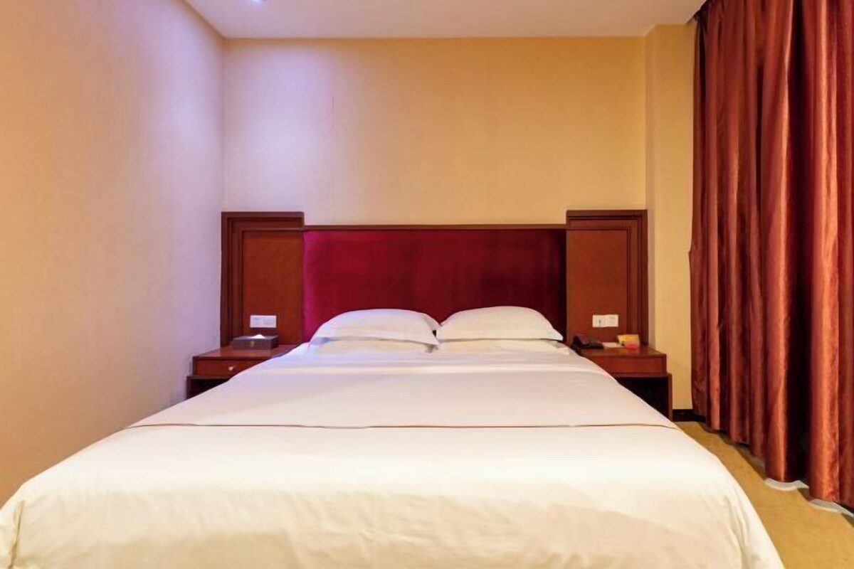 Una habitación de hotel con una cama grande, cabecero de madera, dos mesitas de noche y una cortina roja.