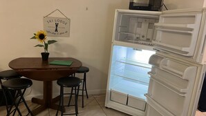 A kitchen with a wooden table, four stools, a refrigerator, and a wall sign. - Comfortable, Within Walking Distance To The Beaches 2217
 (Hallandale Beach)