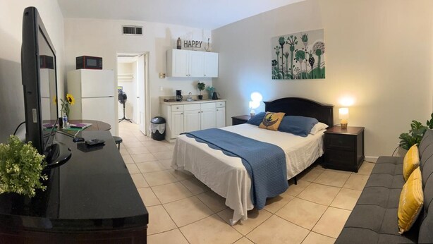 A bedroom with a bed, bedside table, and a TV. There is a kitchen area with cabinets and a microwave. - Comfortable, Within Walking Distance To The Beaches 2217
 (Hallandale Beach)