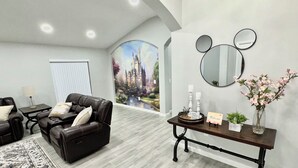 A modern living room with a leather sofa, a coffee table, and a rug. There's a wall with a mural, a mirror, and a vase with flowers.