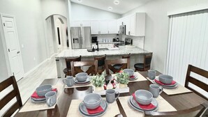 A dining area with a round table set for six, surrounded by wooden chairs.