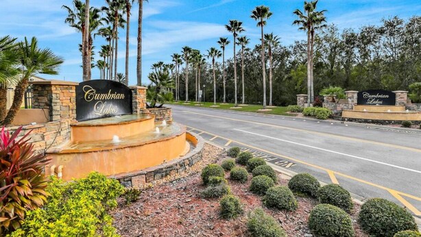 A road leading to a property named 'Cumberland Lakes' with a landscaped area featuring palm trees and a fountain.