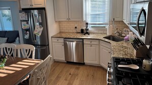 A kitchen with white cabinets, a stainless steel refrigerator, a dishwasher, a granite countertop, a stove, and a sink. - Charming 3-bedroom house in beautiful Cape May, NJ (Cape May)