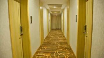 A hotel hallway with carpeted floors, wooden doors, and a ceiling light fixture.