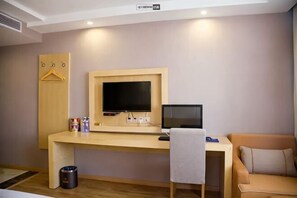 A hotel room with a desk, TV, and couch.