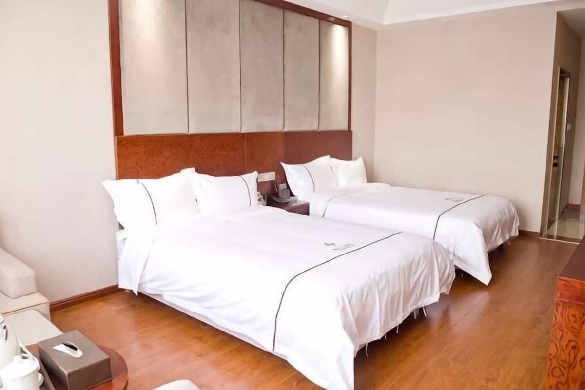 Une chambre d’hôtel avec deux lits, un plancher en bois, une table de chevet et une commode.
