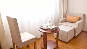 A room with a chair, a sofa, a small table with a tray of items, and a window with curtains. - Fuhao Hotel Suichuan (Suichuan)