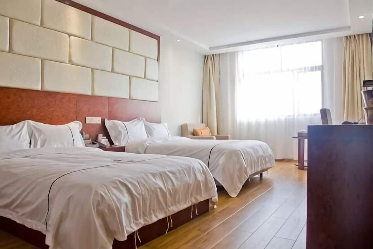 Une chambre d’hôtel avec deux lits, un plancher en bois, une grande fenêtre avec des rideaux et un bureau avec une chaise.