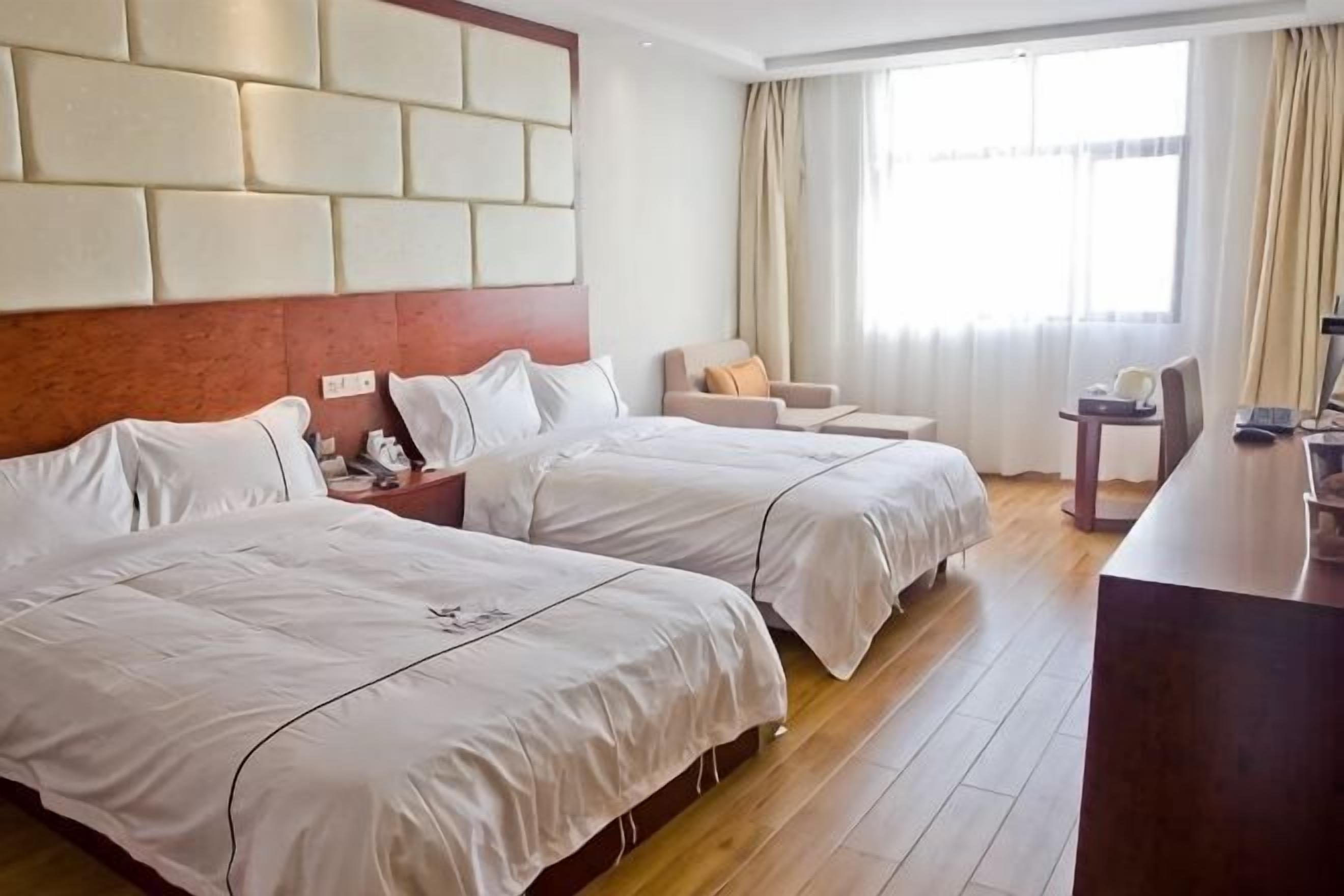 A hotel room with two beds, a desk, a chair, and a large window.